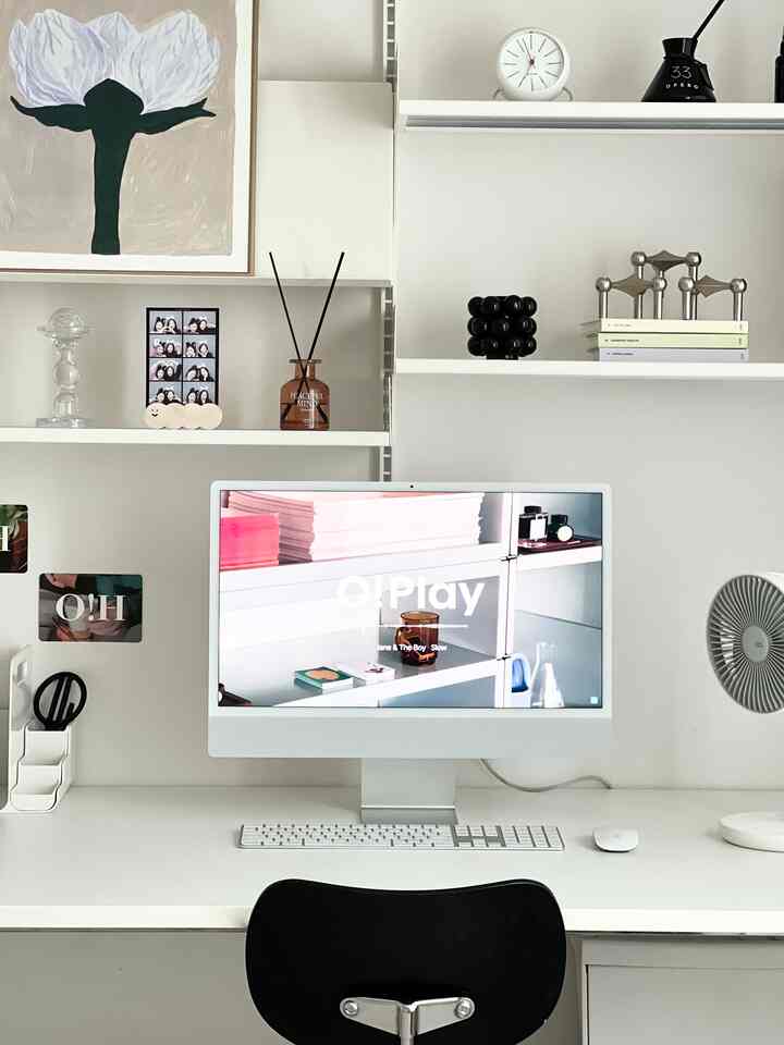 White-toned compact home office featuring an iMac, desk, shelves with decor, and a modern minimalist interior