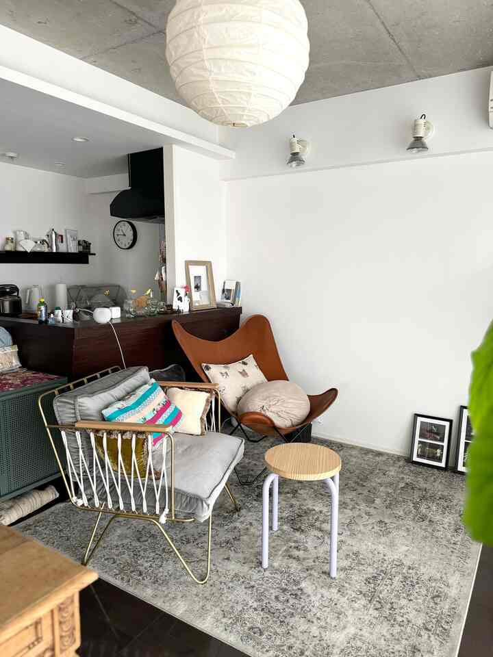 白壁とコンクリート天井が調和するリビング、ブラウンレザーのアームチェアとライトウッドのスツール、グレーのヴィンテージラグが配置されたナチュラルモダンなインテリア