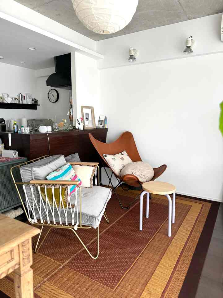 Natural color and white toned living room featuring gray armchair, brown leather butterfly chair, round stool, and large brown rug in a simple setting