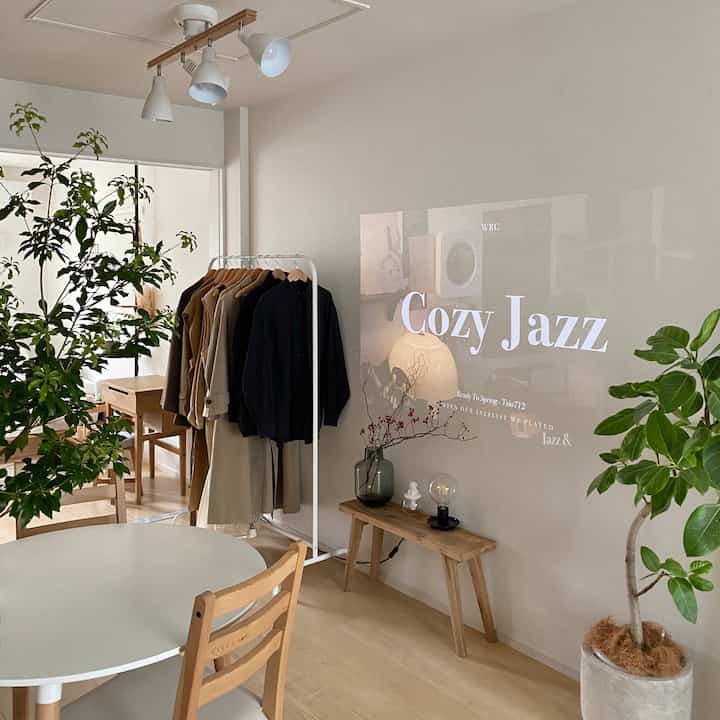 白と木目調が調和した二人暮らし向けのリビング、衣類ハンガーとダイニングチェアが配置されたシンプルで自然な印象の空間