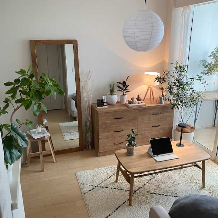 ナチュラルトーンのリビングルーム、木製のコーヒーテーブルとチェスト、多様な室内植物が配置された清潔で落ち着いた空間