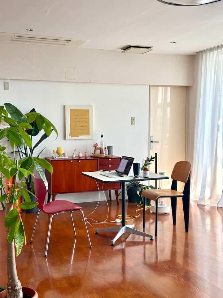 白い壁と茶色い木の床が特徴の北欧風ワークスペース、ダイニングテーブルと椅子、緑の植物が配置された落ち着いた空間