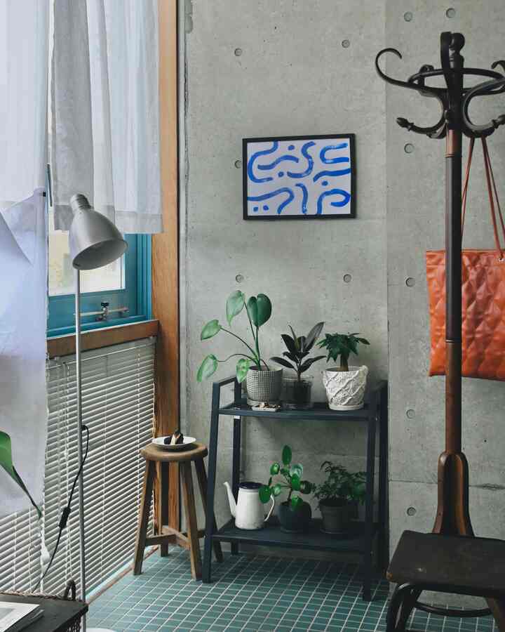 緑と黒のトーンが調和した植物コーナー、棚と木製スツール、ブラインドが配置された落ち着いた雰囲気のインテリア