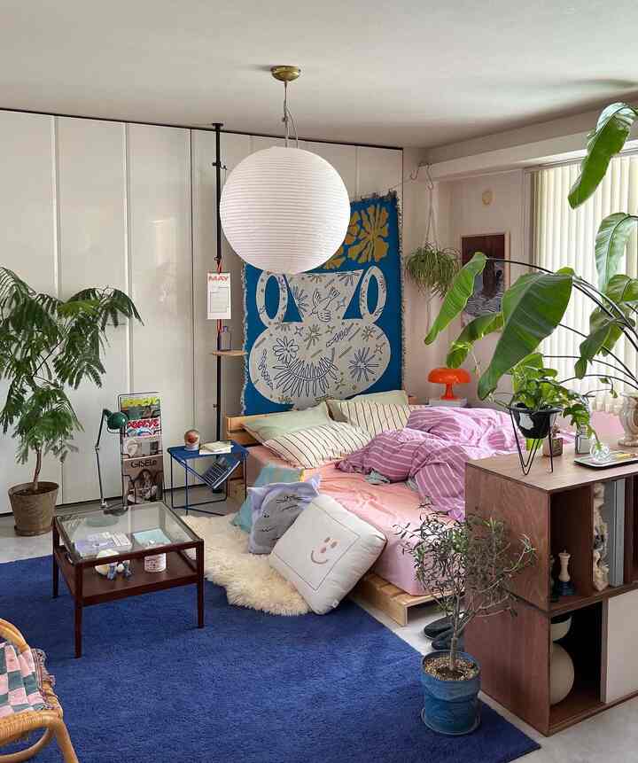 Beige-toned bedroom featuring wooden bed with colorful bedding and multiple plants creating a cozy atmosphere
