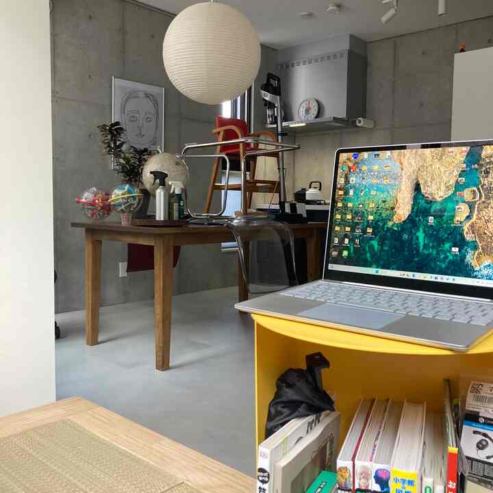 Natural wood tones and transparent elements in a studio apartment dining room, featuring a yellow shelf with laptop creating a tidy remote work setup