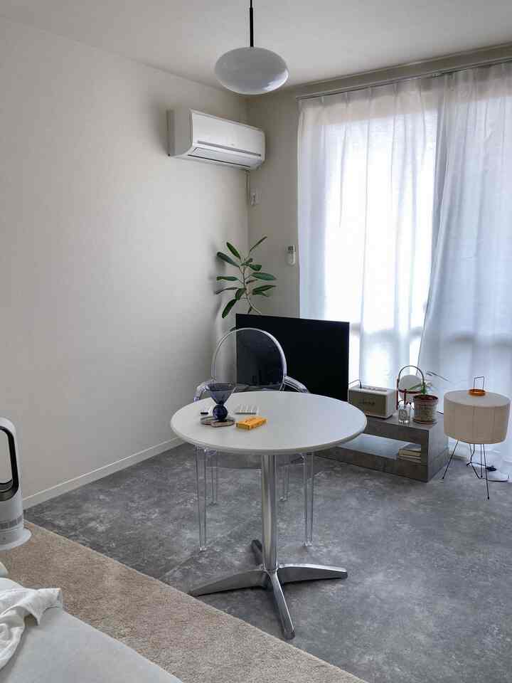 明るい白とグレーのトーンの一人暮らし用リビング、丸いテーブルと透明なチェアが配置されたシンプルでモノトーンな雰囲気のインテリア