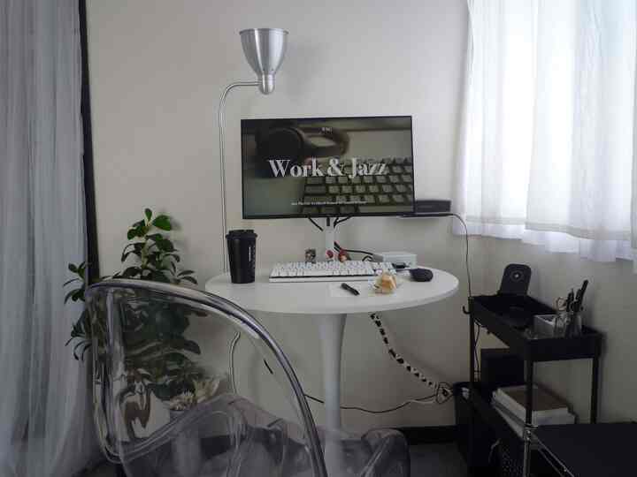 White and monotone small home office featuring a transparent chair and simple round desk with a clean work setup