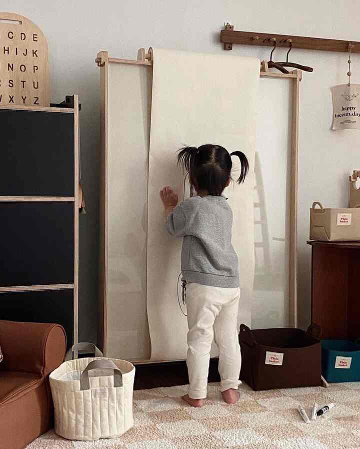 Beige and white toned kids' room featuring a rug, storage baskets, and a child drawing on a large paper roll, creating a natural atmosphere