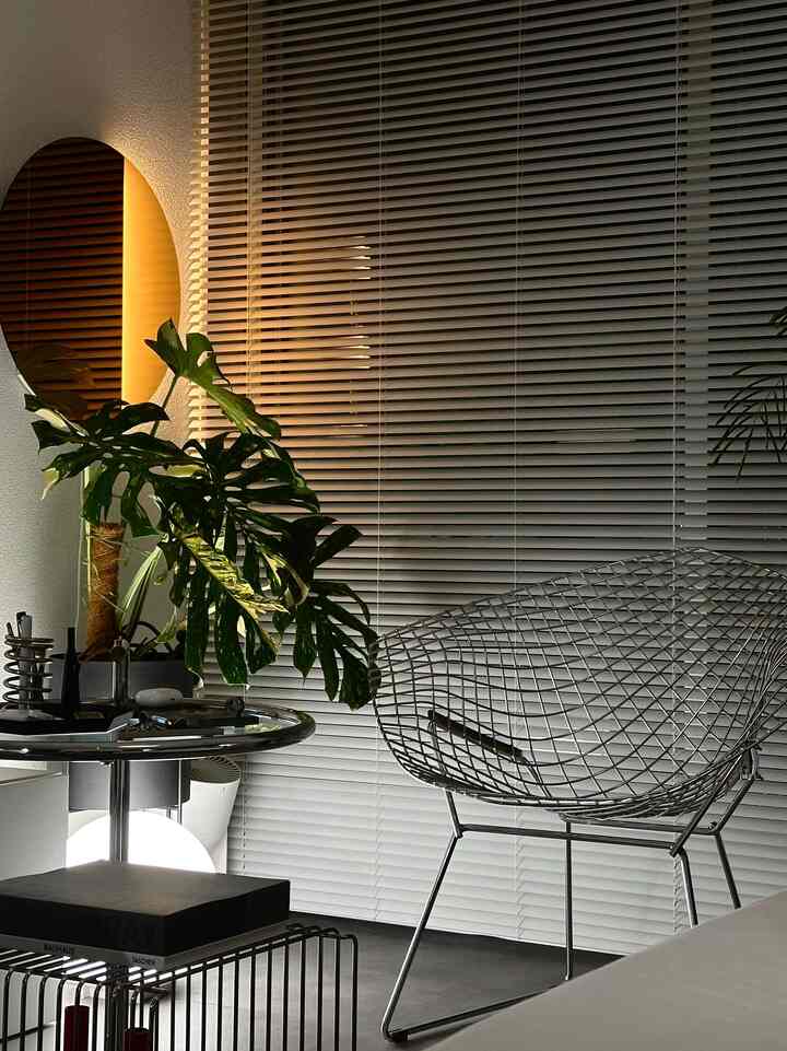 白とグレーのトーンのリビング、モダンな金属製チェアとブラインドが調和したシンプルモダンな空間