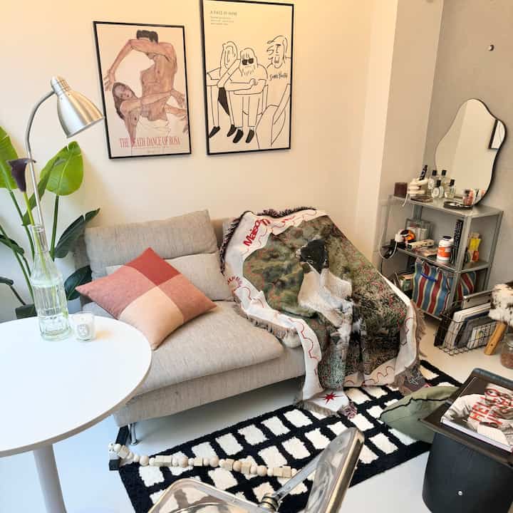 Natural modern living room with beige sofa and white round table, two framed wall arts above sofa, silver floor lamp and green plants creating warm atmosphere