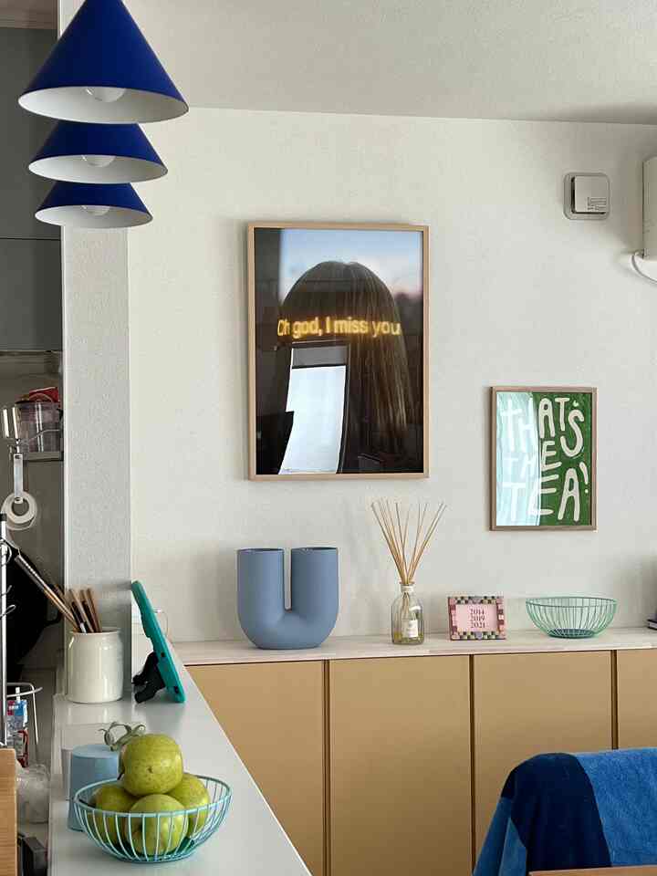 白い壁と木目調のキャビネットがあるダイニング、青いペンダントライトとポスターが配された落ち着いた雰囲気のあるインテリア