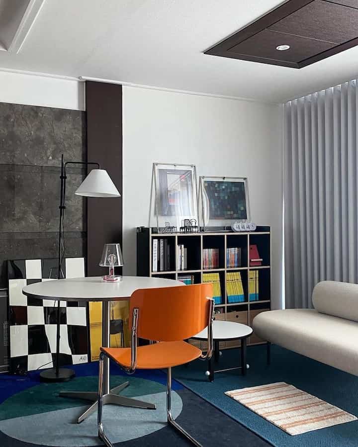 白とオレンジのトーンのリビングルーム、丸テーブルとソファ、本棚が温かみのあるモダンなインテリアを演出