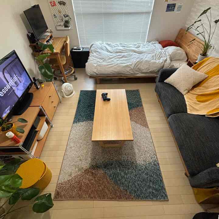 ナチュラルカラーとイエローのアクセントが映える7畳の1Kワンルーム、ソファとベッドが配置された雰囲気のあるインテリア