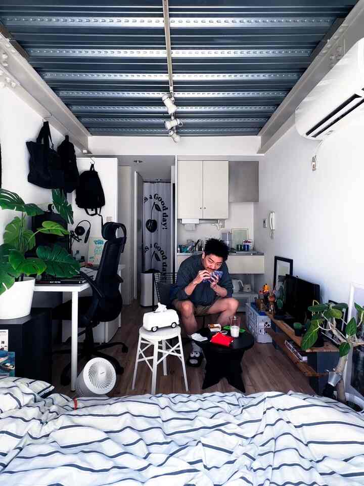 White and gray toned studio apartment bedroom featuring desk, office chair, and multiple plants with cozy atmosphere