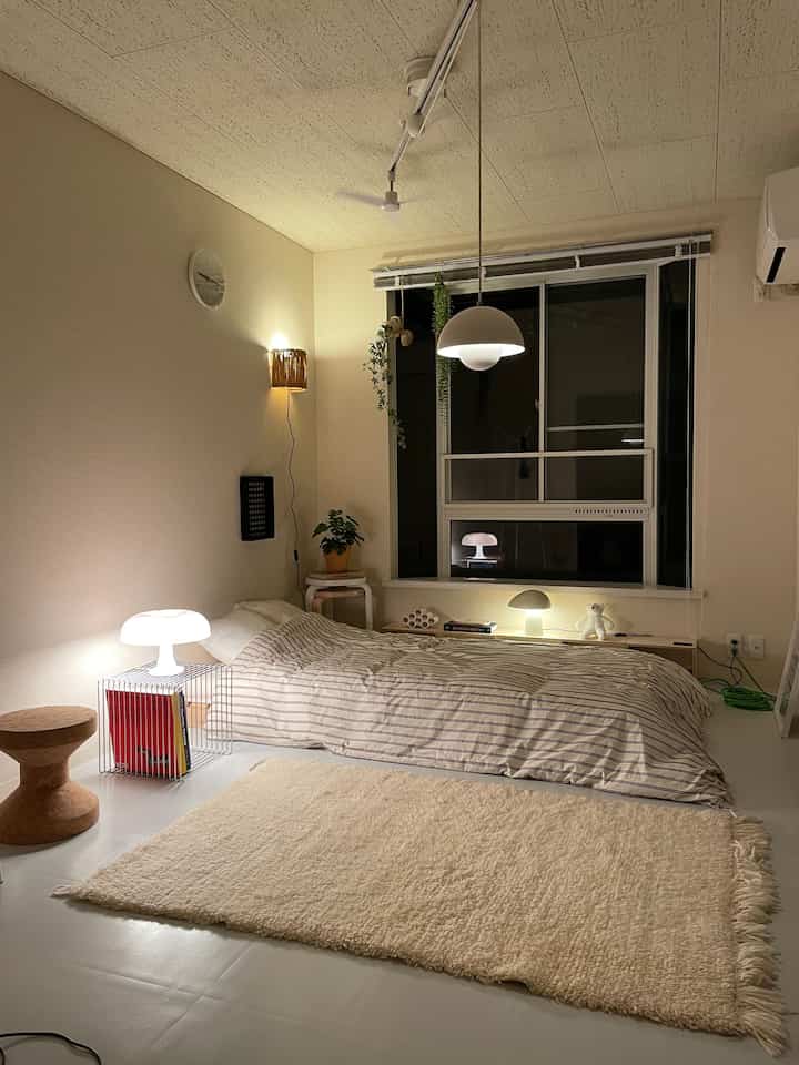 Beige walls and white floor bedroom featuring low bed on floor and multiple table lamps creating cozy indirect lighting atmosphere