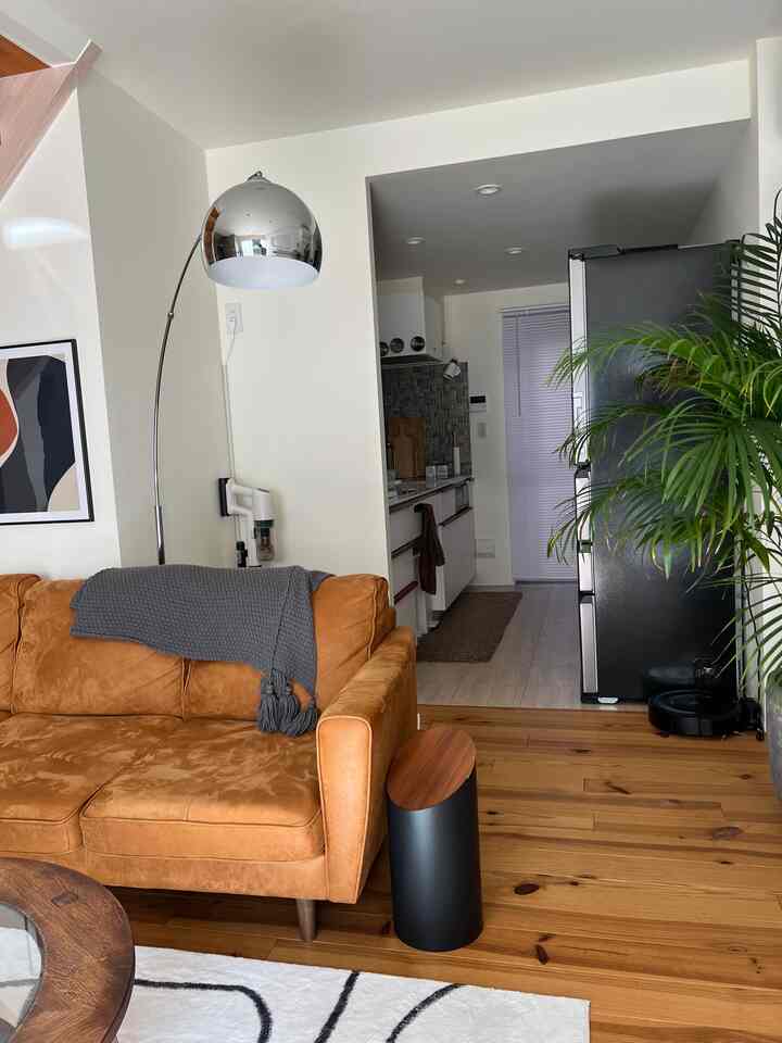 白い壁と木目調の床が調和したモダンなリビング、オレンジ色のソファとメタリックなフロアランプが配置された印象的な空間