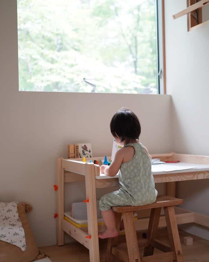 ナチュラルトーンの子供部屋、木製の子供用机とスツールに座って遊ぶ子供がいる落ち着いた空間