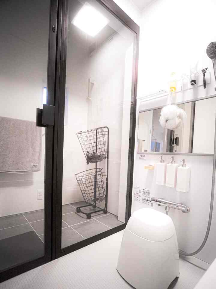 白を基調としたバスルーム、マグネットディスペンサーと黒い収納バスケットが配置されたシンプルな空間