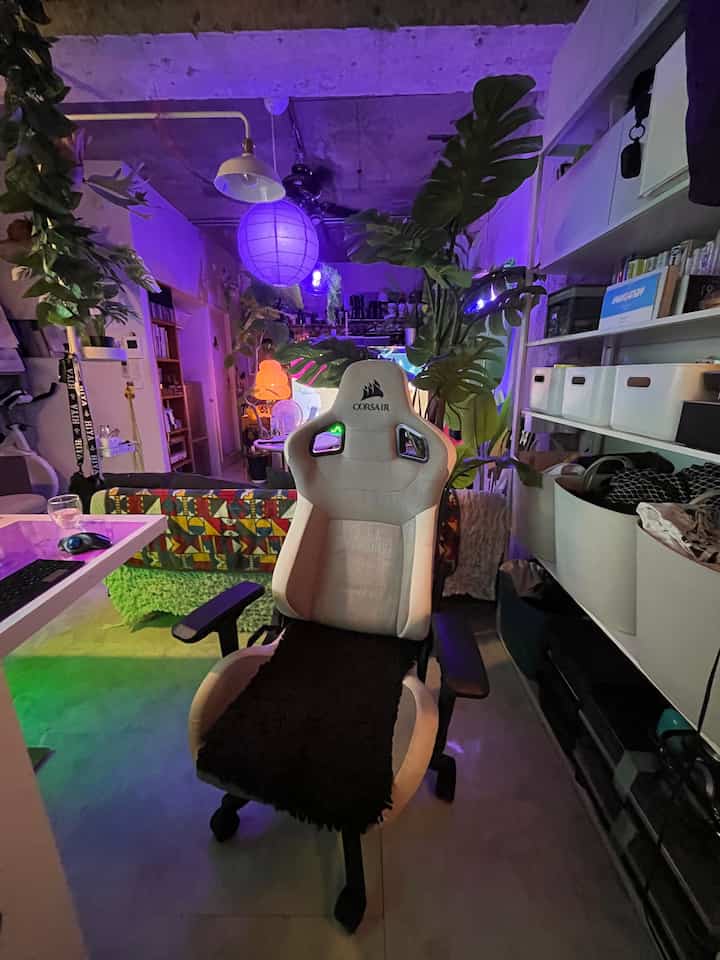 ネオンライトの紫色が漂うインダストリアルなワンルーム、ホワイトの収納ボックスとゲーミングチェア、植物のあるバルコニーが特徴の空間