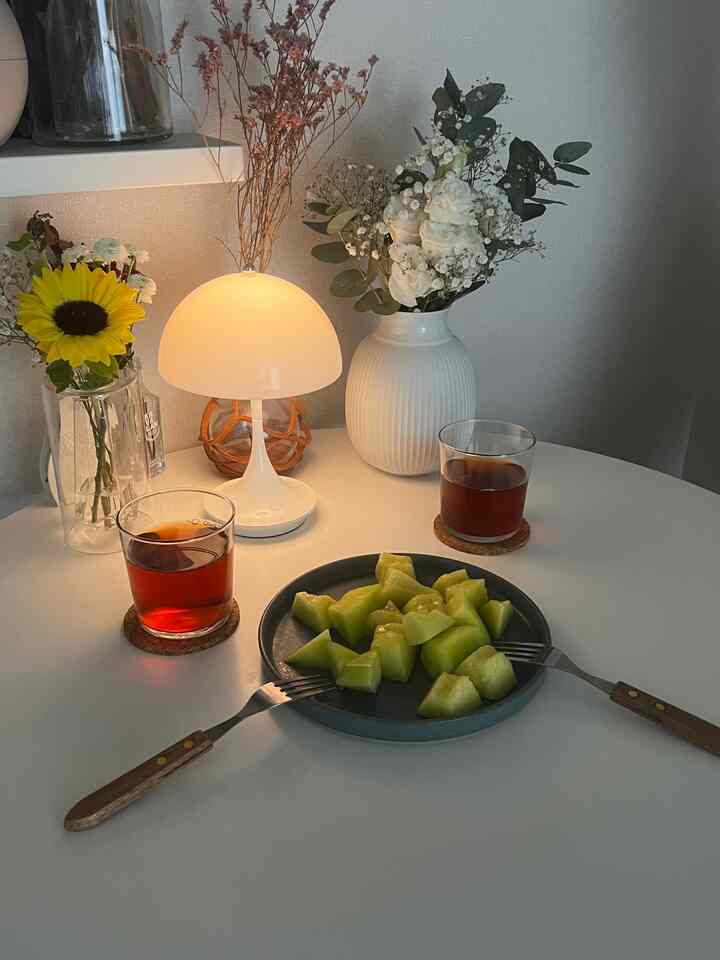 White-toned studio apartment space featuring a table lamp and plate with melon pieces, showcasing a natural interior design
