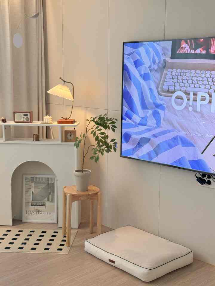 白とベージュの色調のリビングルーム、大型テレビとペットベッド、モビールとフロアランプが配置された雰囲気のあるインテリア