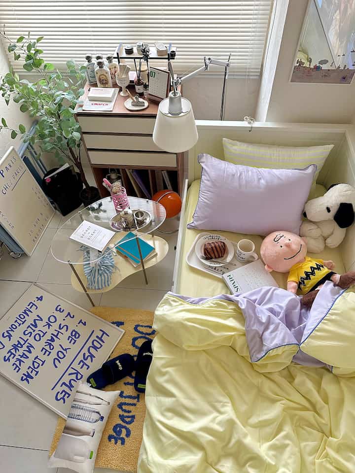 明るいホワイトトーンの寝室、ホワイトベッドとラベンダークッション、デスクランプが配置された雰囲気のある空間