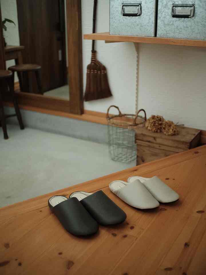 ナチュラルな木目調の玄関、木製のベンチに2色のスリッパと金属製ワイヤーバスケットが置かれたミニマルな雰囲気のインテリア