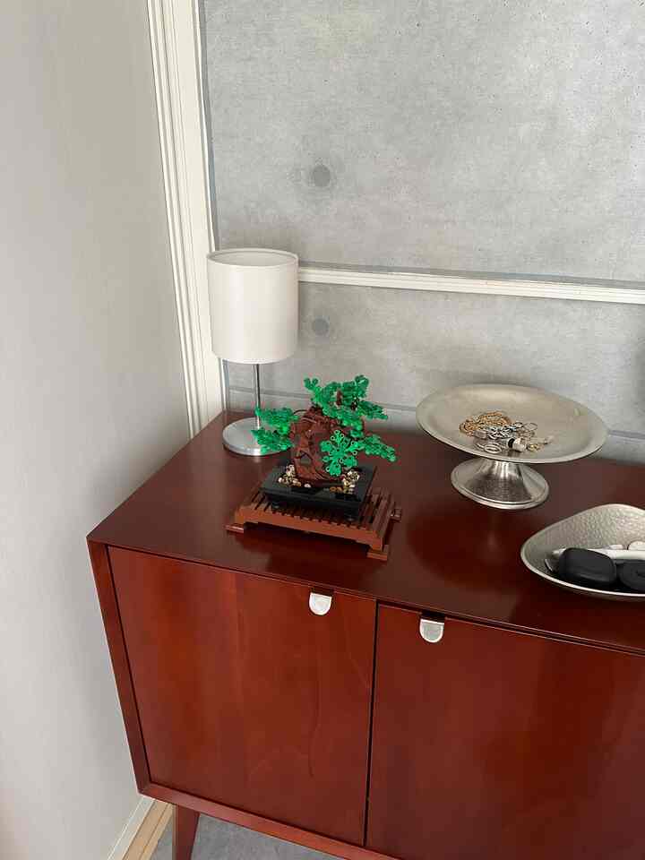 Industrial-style corner wood tone cabinet featuring white lamp and LEGO bonsai plant on top