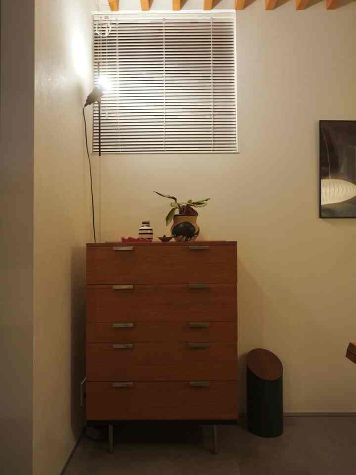 ベージュ色の壁とブラウンのチェストが配置されたシンプルでナチュラルなリビングの雰囲気あるインテリア