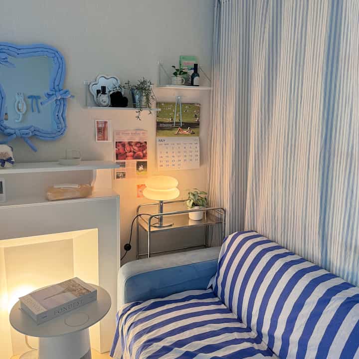 パステルブルーとベージュの色調のリビング、ストライプのソファとトロリーの上のテーブルランプが配置された雰囲気のある空間