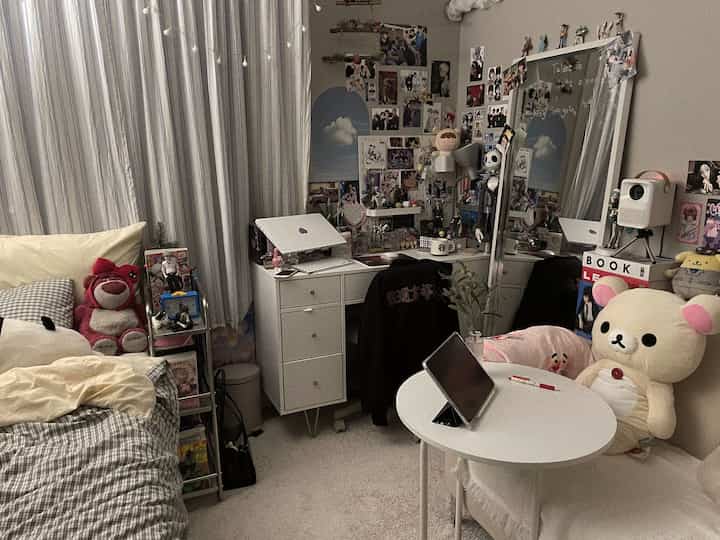 ベージュとホワイトのトーンの狭い寝室、デスクとソファ、キャラクターのぬいぐるみが配置された居心地の良い一人暮らしの空間