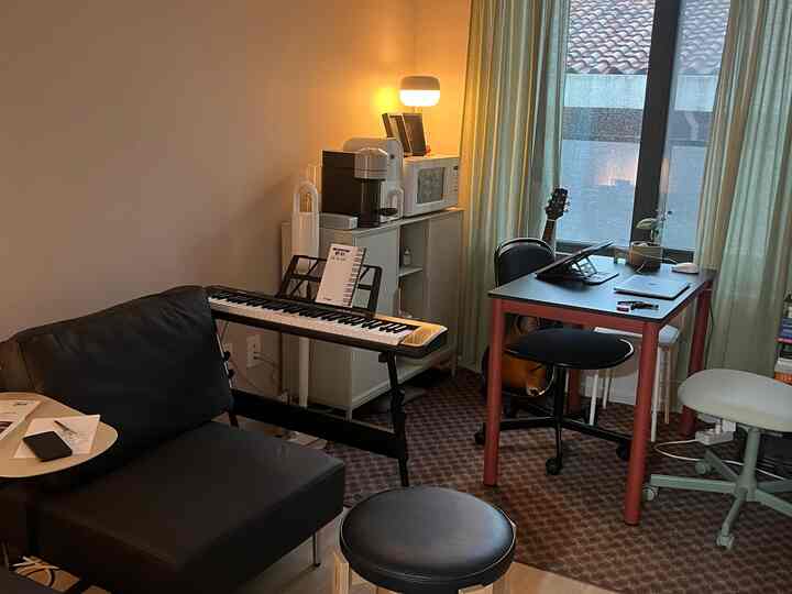 黒と白の小さな一人暮らし用ホームオフィス空間、デジタルピアノとデスク、ソファが配置された落ち着いた雰囲気のインテリア