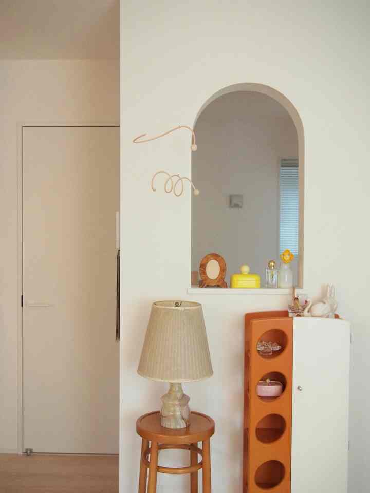 ナチュラルな色調の4.5畳の部屋、アーチ型の室内窓と木製スツール、ベージュ色のランプが配置された雰囲気のあるインテリア