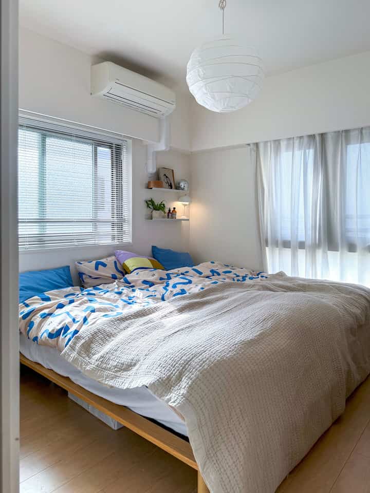 白と木目調の色調の寝室、広いベッドと明るいカーテン、ペンダントライトが配置された雰囲気のあるインテリア