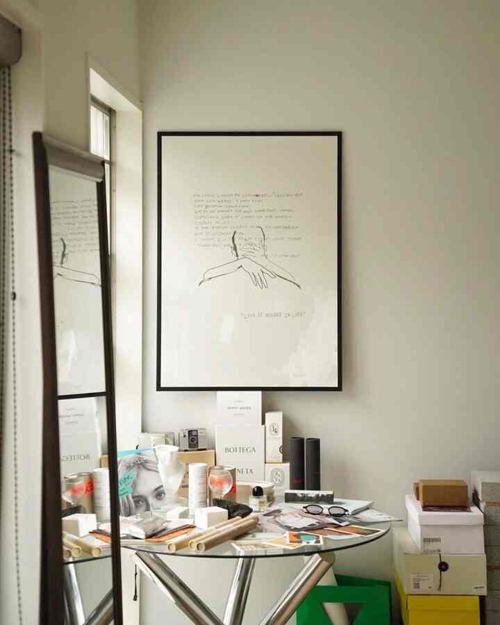 透明な丸いガラステーブルとブラウンフレームの鏡、白い壁にポスターが掛かった印象的な玄関空間