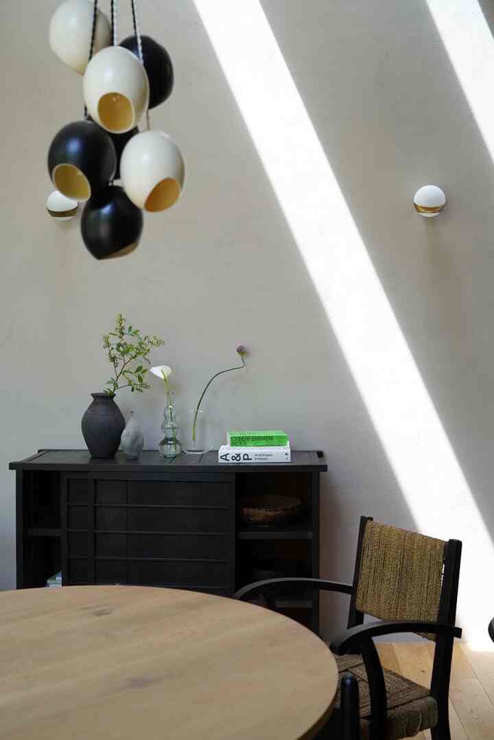 ナチュラルな色調のダイニング、丸い木製テーブルと暗色の収納キャビネットが配置された落ち着いた空間