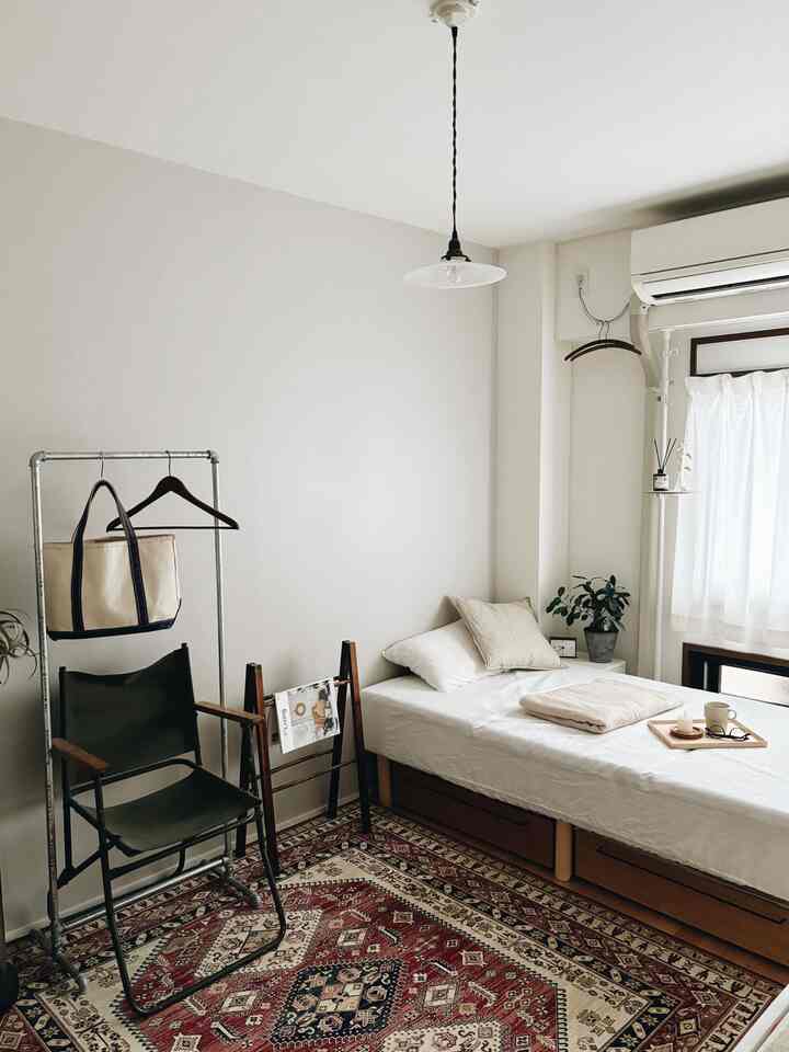 白と茶色の色調の寝室、ベッド下収納とラグが配置されたナチュラルで落ち着いた印象のインテリア