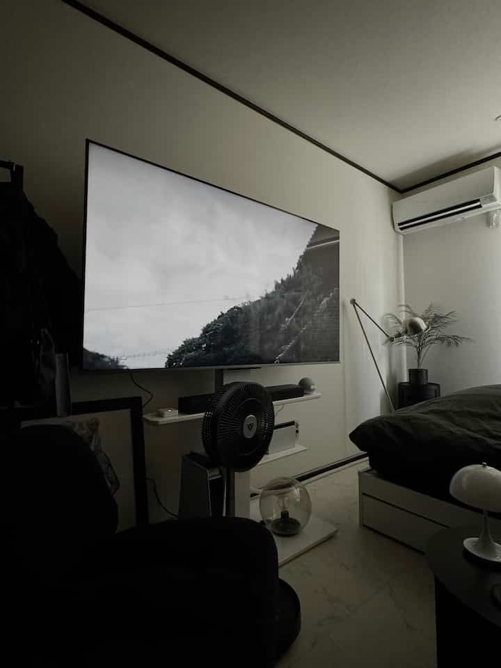 A modern and tidy studio bedroom in white and black tones, featuring a TV and a fan