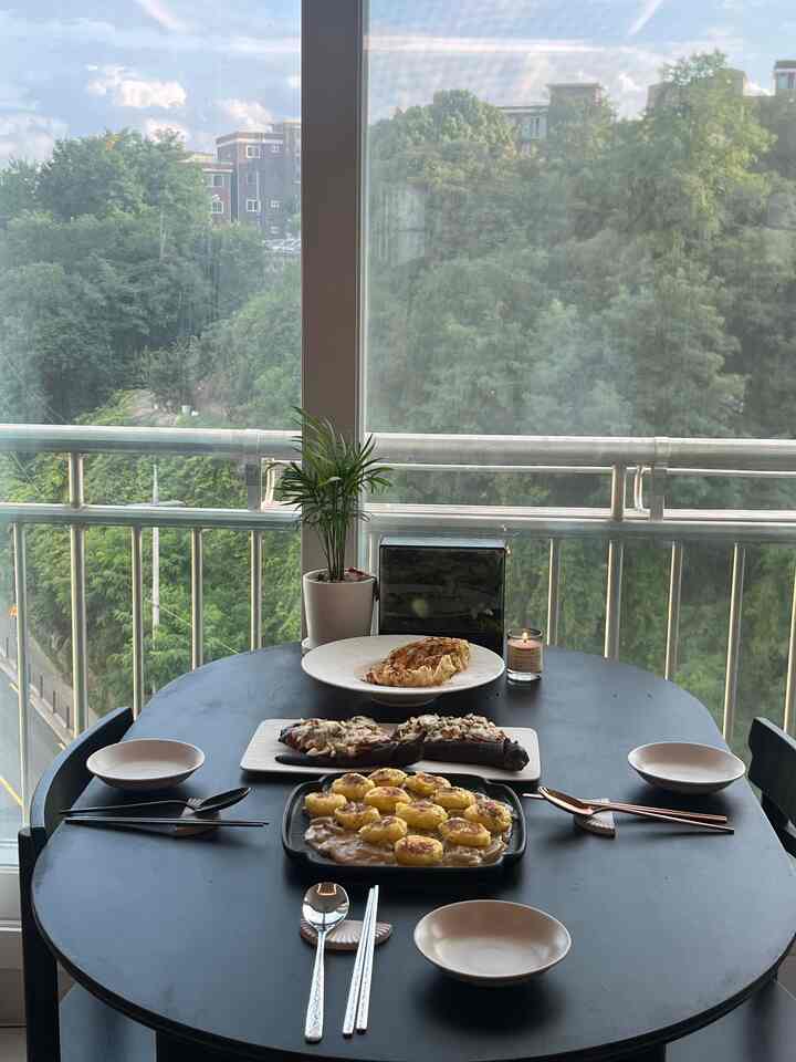 黒を基調としたバルコニーのダイニングスペース、丸いテーブルに4人分の食器と料理が配置され、落ち着いた雰囲気のあるインテリア