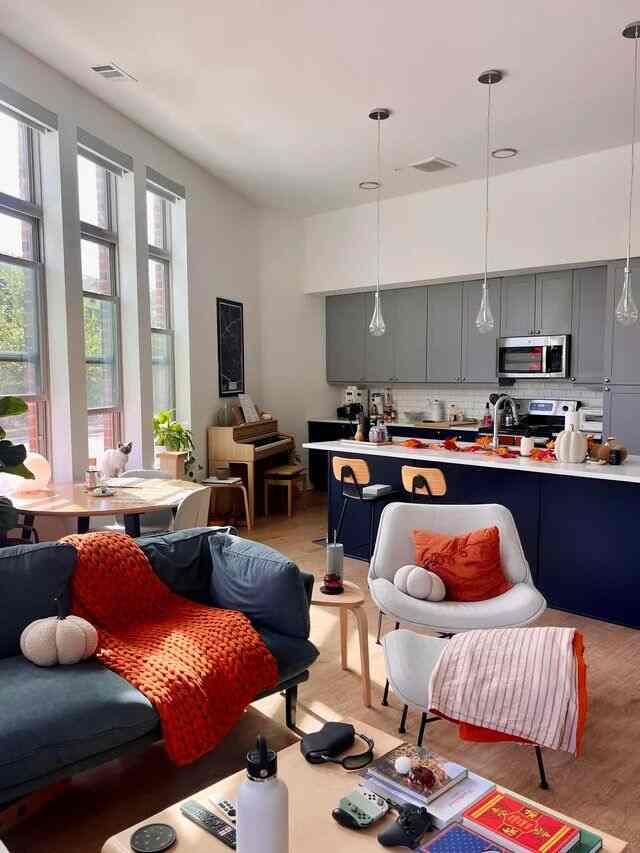 Wood-tone living room with gray kitchen and blue sofa, pendant lights centrally hung, cozy space for living with pets