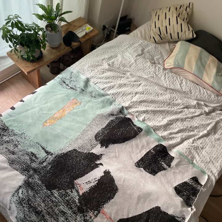 Natural-toned single household bedroom featuring a wooden table with plants and an abstract patterned blanket creating a cozy atmosphere