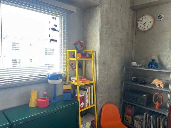 グレーのコンクリート壁と黄色の収納棚があるモダンなホームオフィス空間、オレンジ色の椅子が配置されている
