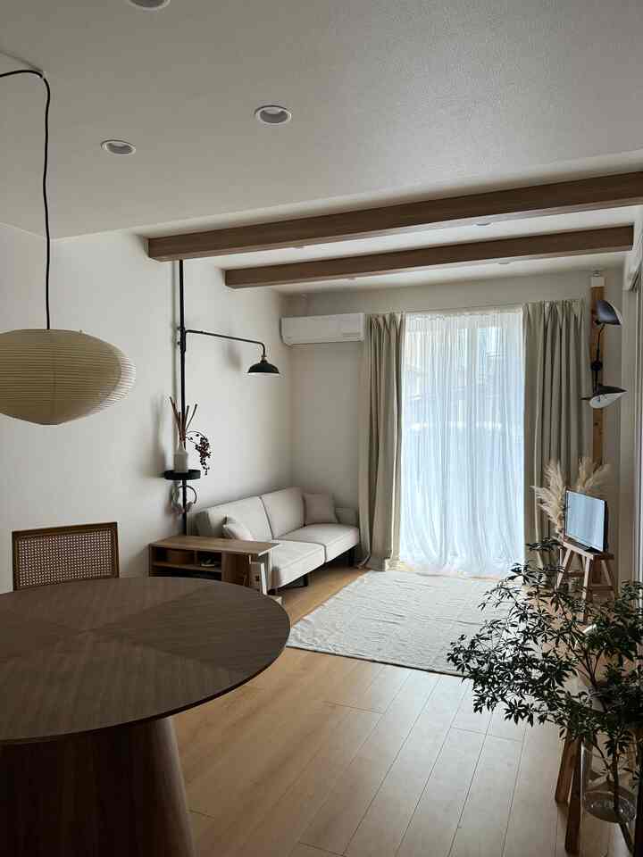 ベージュと木目調のリビング、シンプルなソファと円形のダイニングテーブルが配置された雰囲気のある空間