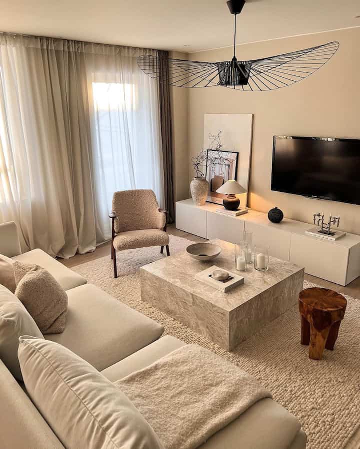 Beige and white toned living room featuring minimal sofa, armchair, and fabric coffee table in harmonious Japandi style