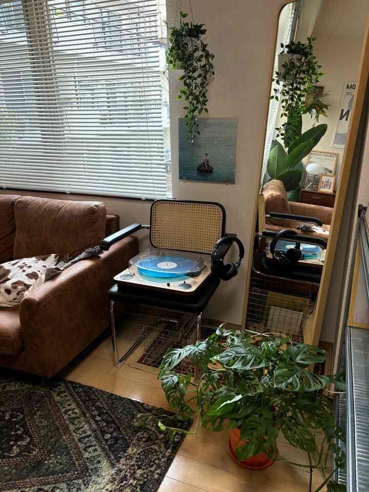ウッドトーンの床とブラウンのソファがあるリビング、ラタンチェアの上にレコードプレーヤーと緑の植物が配置された雰囲気のあるインテリア