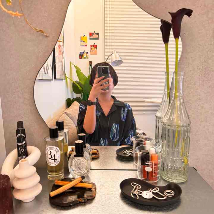 ナチュラルな色調のパウダールーム、独特な曲線の鏡と香水やアクセサリーが配置されたモダンな空間