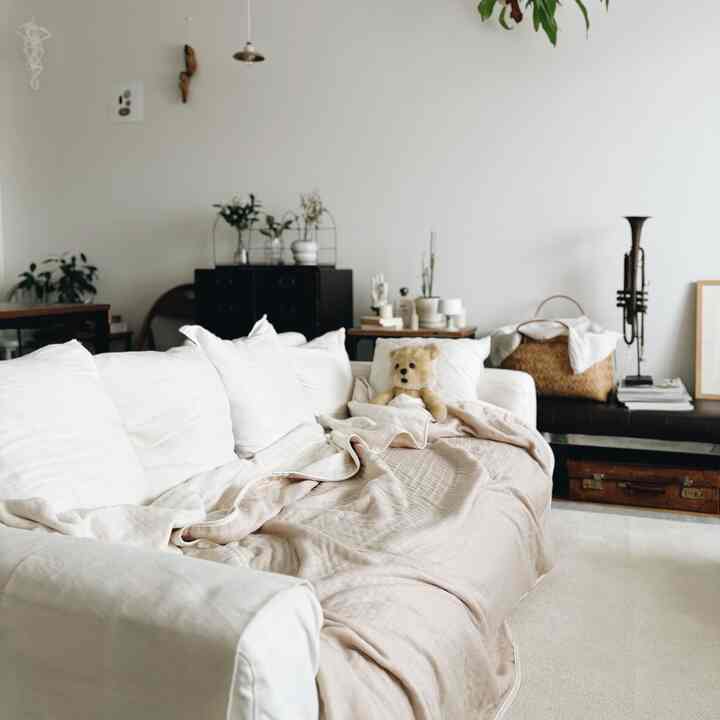 白とベージュの色調のリビング、広いソファにテディベアとガーゼブランケットが配置された落ち着いた雰囲気のインテリア