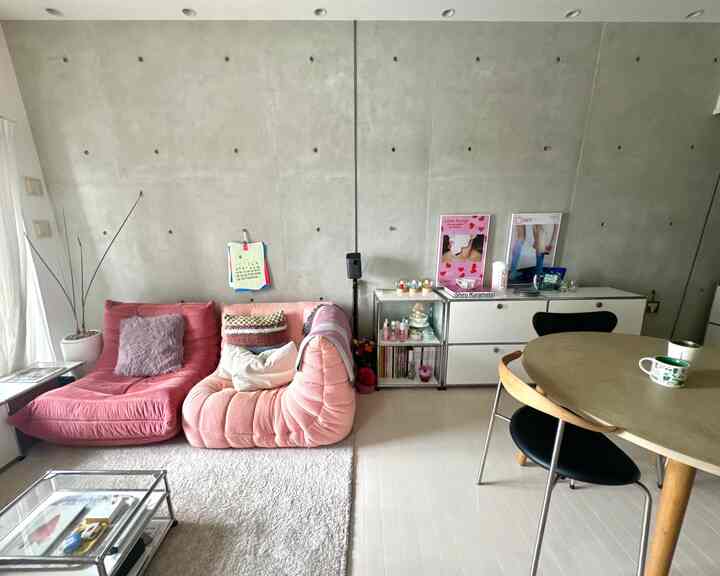 Natural modern living room featuring gray concrete wall, rose gold sofas, and wood-toned dining table creating harmonious space