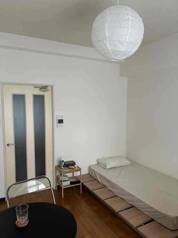 White and beige toned single studio apartment featuring a simple bed and small table with a cozy atmosphere