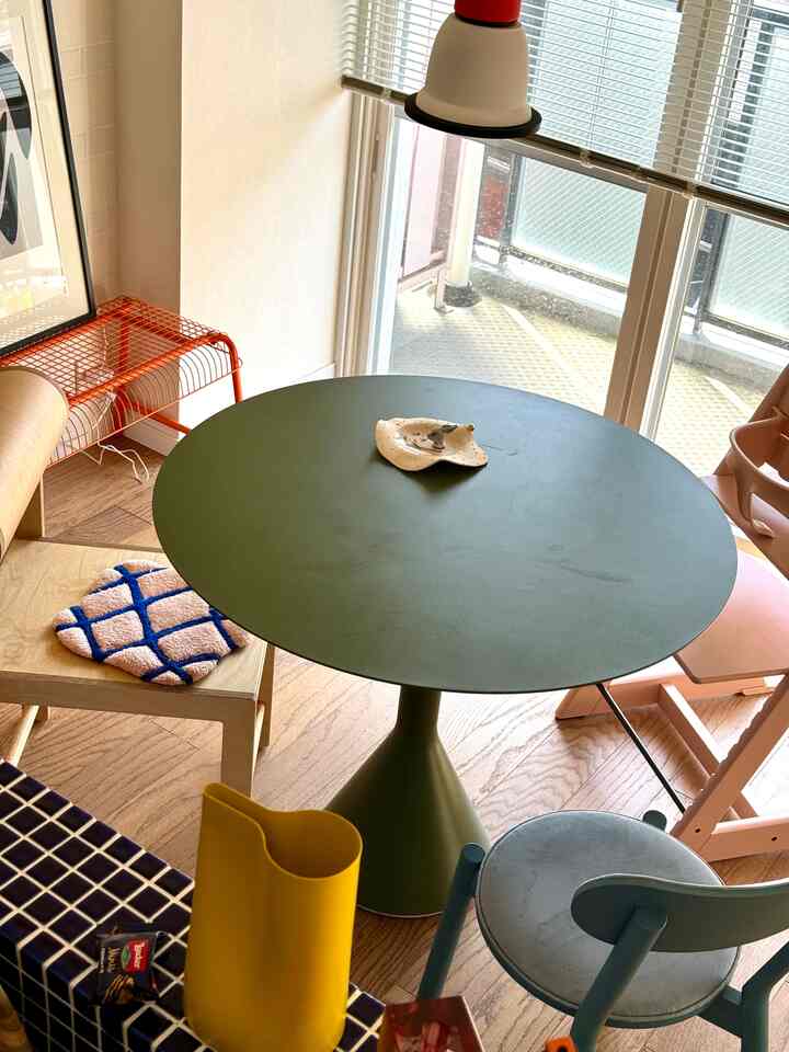 ナチュラルな木目調フロアとグリーンの丸テーブルがあるダイニング、カラフルな椅子とペンダントライトが配置された雰囲気のあるインテリア